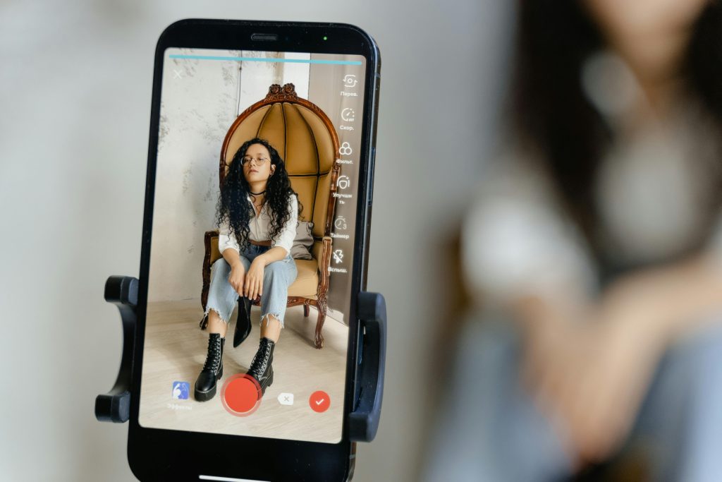 A woman sits in a chair recording a video on her smartphone, showcasing modern vlogging techniques.